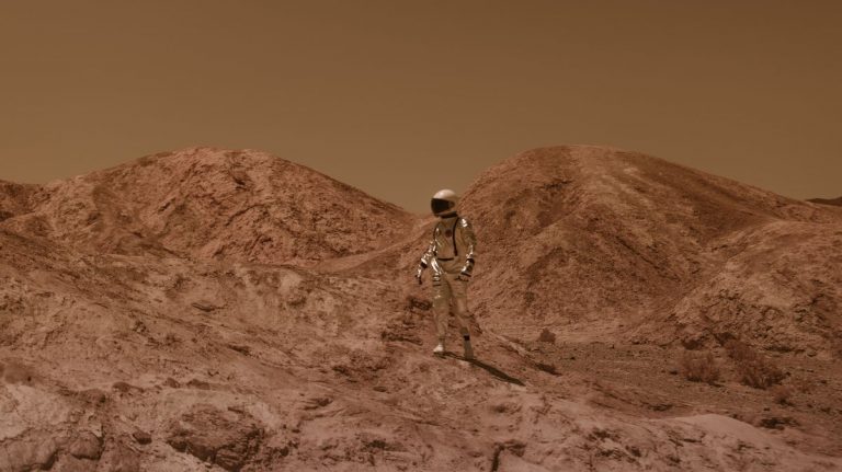 Astronaut in spacesuit explores barren, Mars-like desert terrain under brown sky