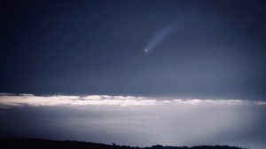 Astounding view of a luminous comet streaking across a starry night sky above a cloud layer