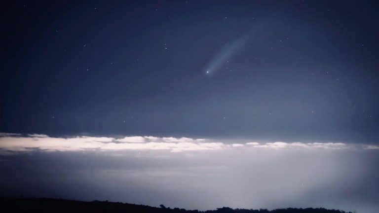 Astounding view of a luminous comet streaking across a starry night sky above a cloud layer