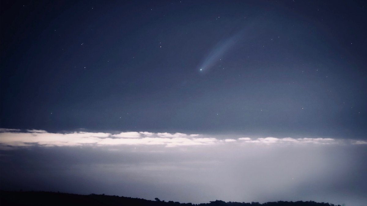 Astounding view of a luminous comet streaking across a starry night sky above a cloud layer