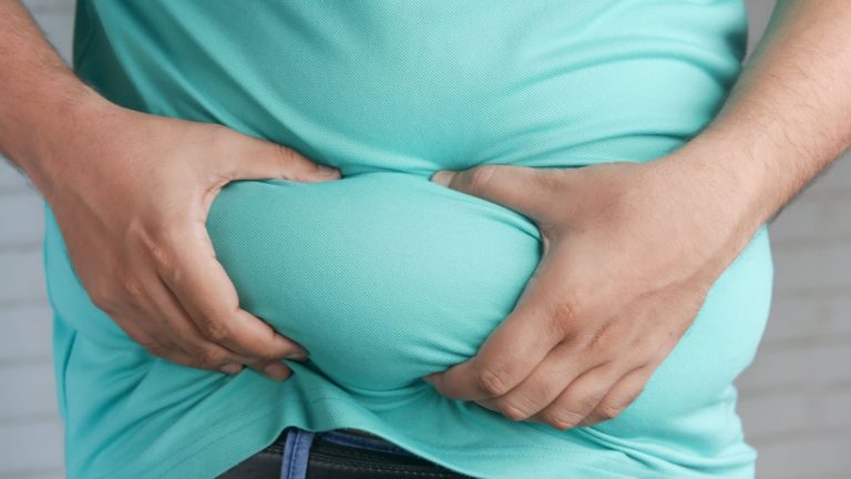 Close-up of hands gripping an overweight belly, depicting body fat focus