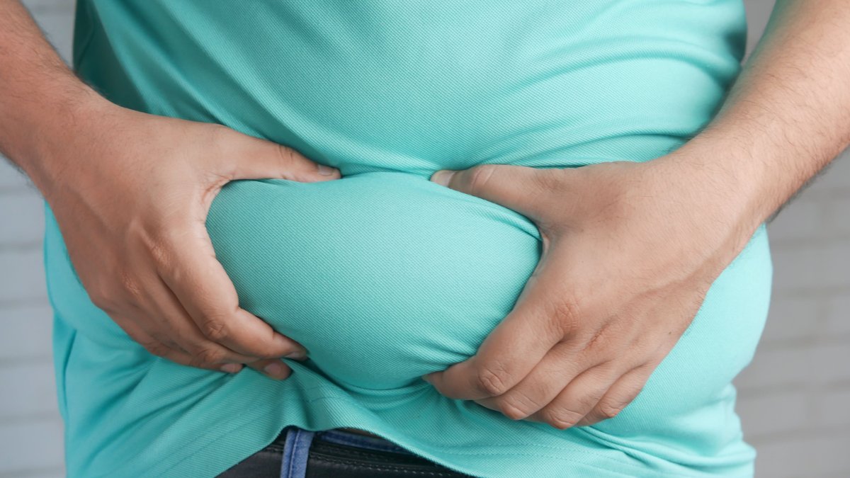 Close-up of hands gripping an overweight belly, depicting body fat focus