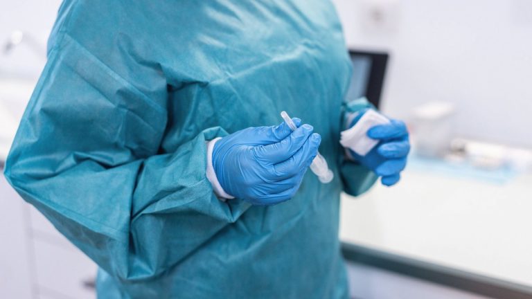 Medical doctor holding syringe with vaccine for coronavirus disease - Focus on right hand glove