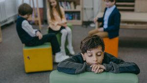 Child feeling isolated in a classroom while peers interact. Emphasizes themes of loneliness and social dynamics