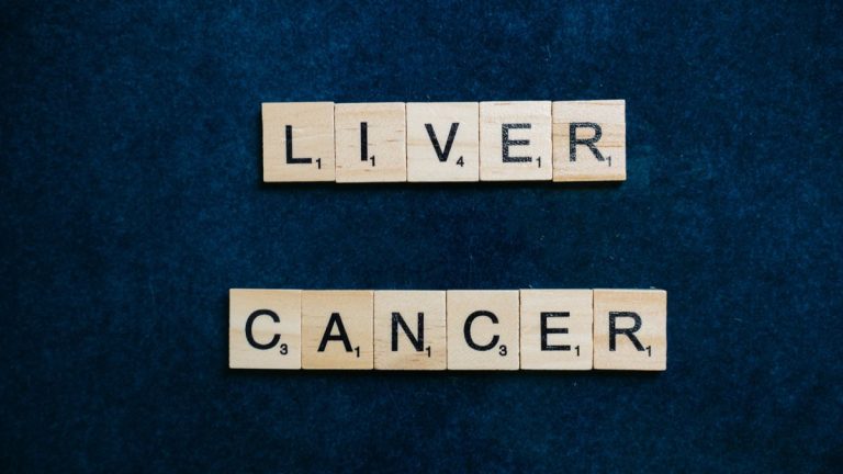 Scrabble tiles spell out 'Liver Cancer' on a dark blue background, symbolizing awareness