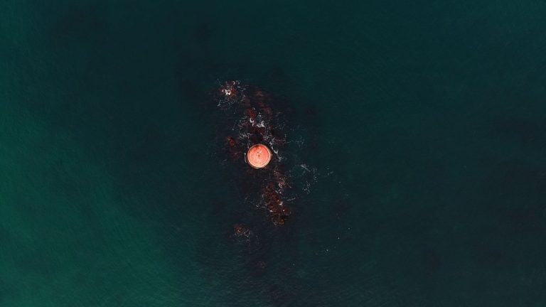 A serene top-down shot of a buoy floating in tranquil ocean waters, showcasing vivid blues and greens