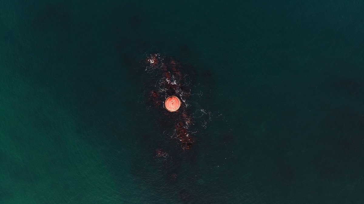 A serene top-down shot of a buoy floating in tranquil ocean waters, showcasing vivid blues and greens