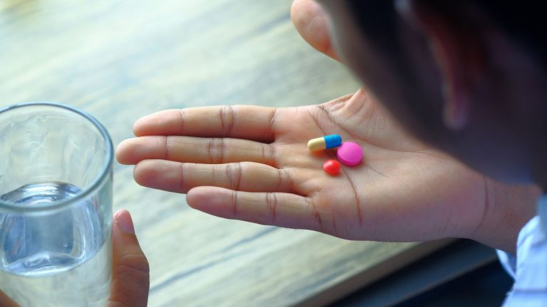 Hand holding medication pills beside a glass of water