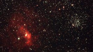 Vibrant photograph of the starry night sky featuring a bright red nebula and star clusters