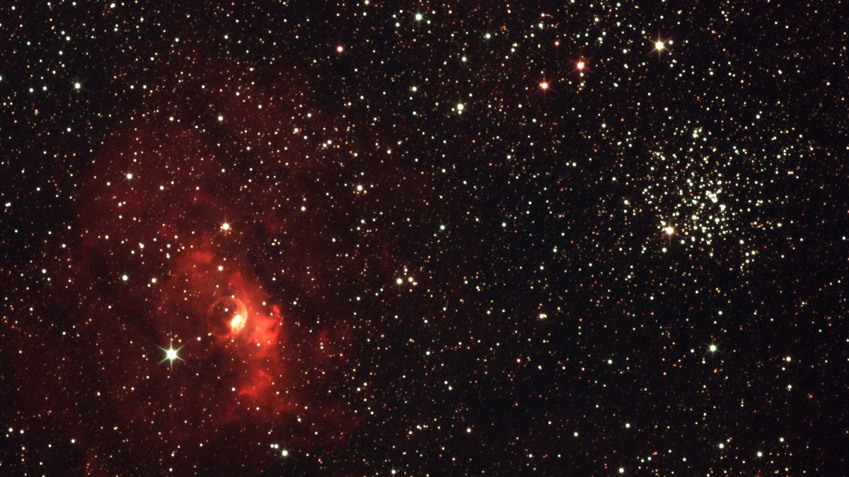Vibrant photograph of the starry night sky featuring a bright red nebula and star clusters