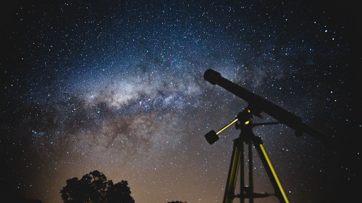 Telescope under a starry sky used to illustrate the search for distant outer solar system objects