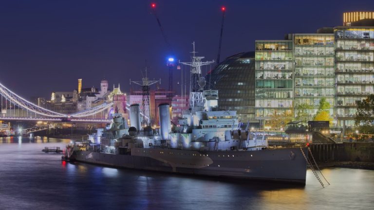 Illuminated HMS Belfast with Tower Bridge in the backdrop at night in London