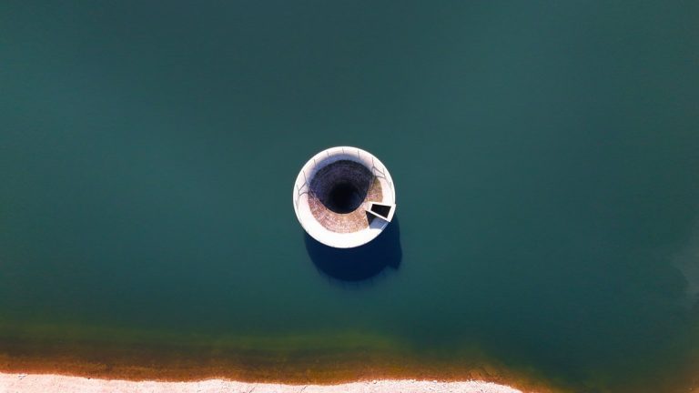 Aerial shot of a circular spillway surrounded by deep green water in a reservoir