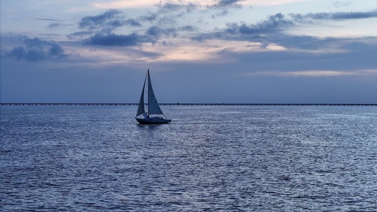 A sailboat glides peacefully across Lake Pontchartrain under a picturesque sunset sky