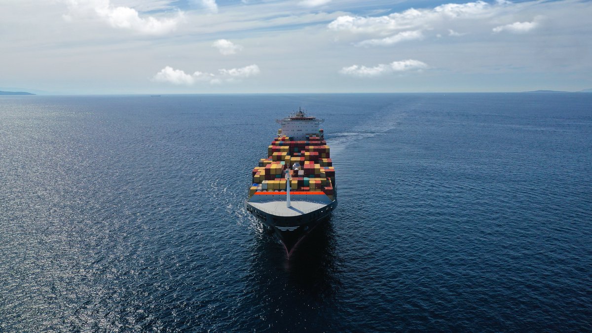 Aerial drone photo of huge container tanker ship carrying truck size colourful containers in deep blue open ocean sea
