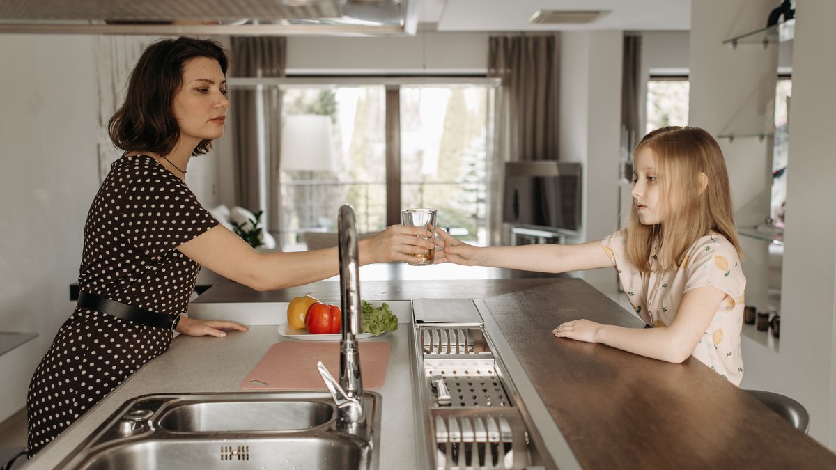 A mother and daughter bonding over a glass of water in a modern kitchen setting