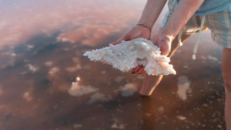 Close-up of hands holding salt crystals from a shallow saline lake at sunset