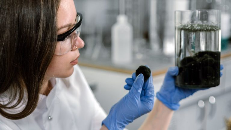 A scientist in a lab coat examines a sample with laboratory equipment