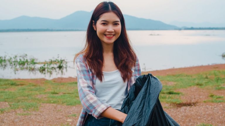 Portrait of young Asia lady volunteers help to keep nature clean up holding plastic bottle waste and black garbage bags on the beach. Concept about environmental conservation pollu