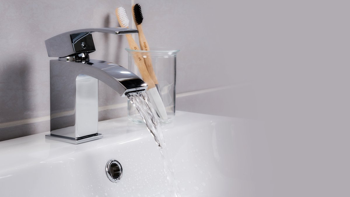 A closeup shot of water flowing from a basin mixer tap in the bathroom
