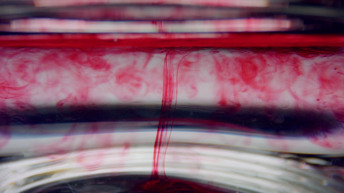 Closeup test tube with blood sample. Clear liquid mixing with red chemical reagent. Macro of blood drops flowing in water. Coronavirus vaccine research in scientific lab