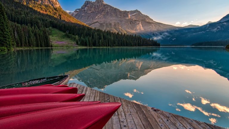 Vibrant red canoes on Emerald Lake with stunning mountain reflections at sunrise in British Columbia