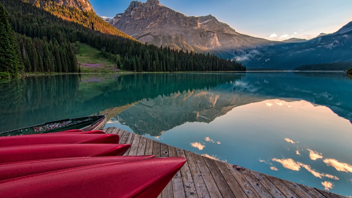 Vibrant red canoes on Emerald Lake with stunning mountain reflections at sunrise in British Columbia