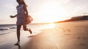 Happy little girl running on the beach at sunset - Kid having fun in holiday vacation with back sun light - Youth, lifestyle and happiness concept - Focus on silhouette