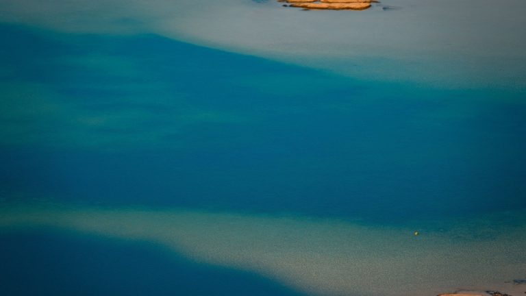A serene aerial shot capturing the tranquil turquoise waters of a lake under the sunlight