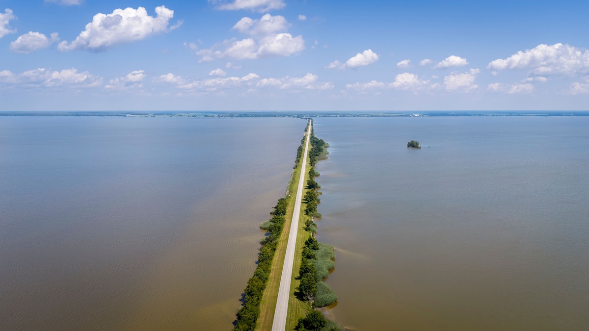 A striking aerial photograph of a long road stretching through a vast lake on a sunny day