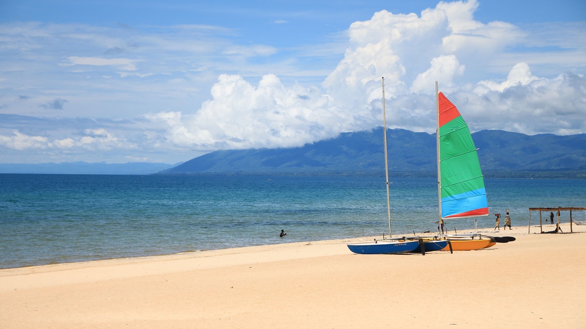 Vibrant sailboats rest on a sunny Lake Malawi beach with mountains in the background