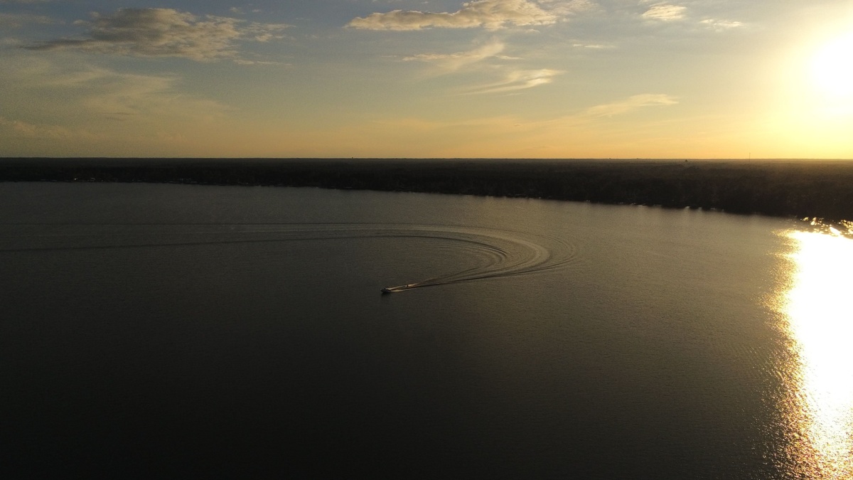 A breathtaking aerial view of a lake at sunset with a motorboat creating ripples, surrounded by a picturesque landscape