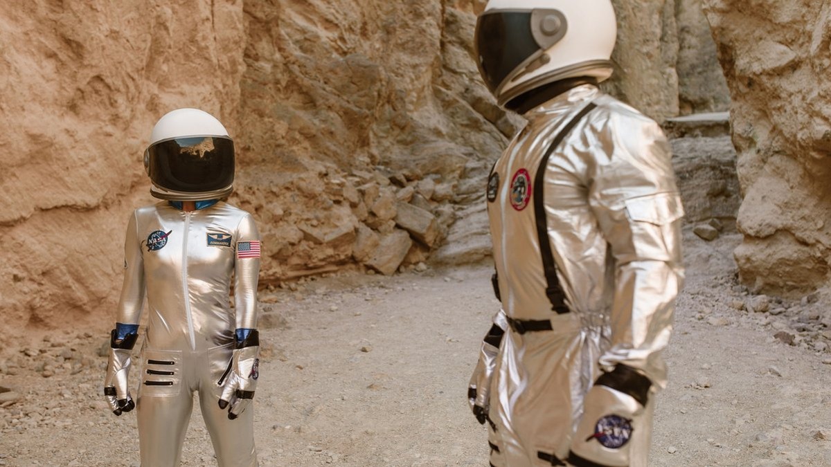 Two astronauts in silver space suits exploring a rocky, desert-like environment, resembling Mars