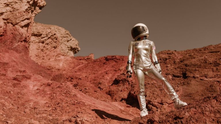 Astronaut in space suit standing on red rocky terrain resembling Mars' surface