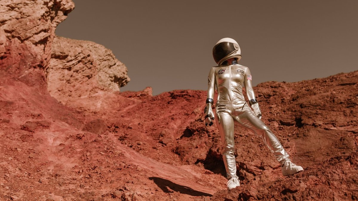 Astronaut in space suit standing on red rocky terrain resembling Mars' surface