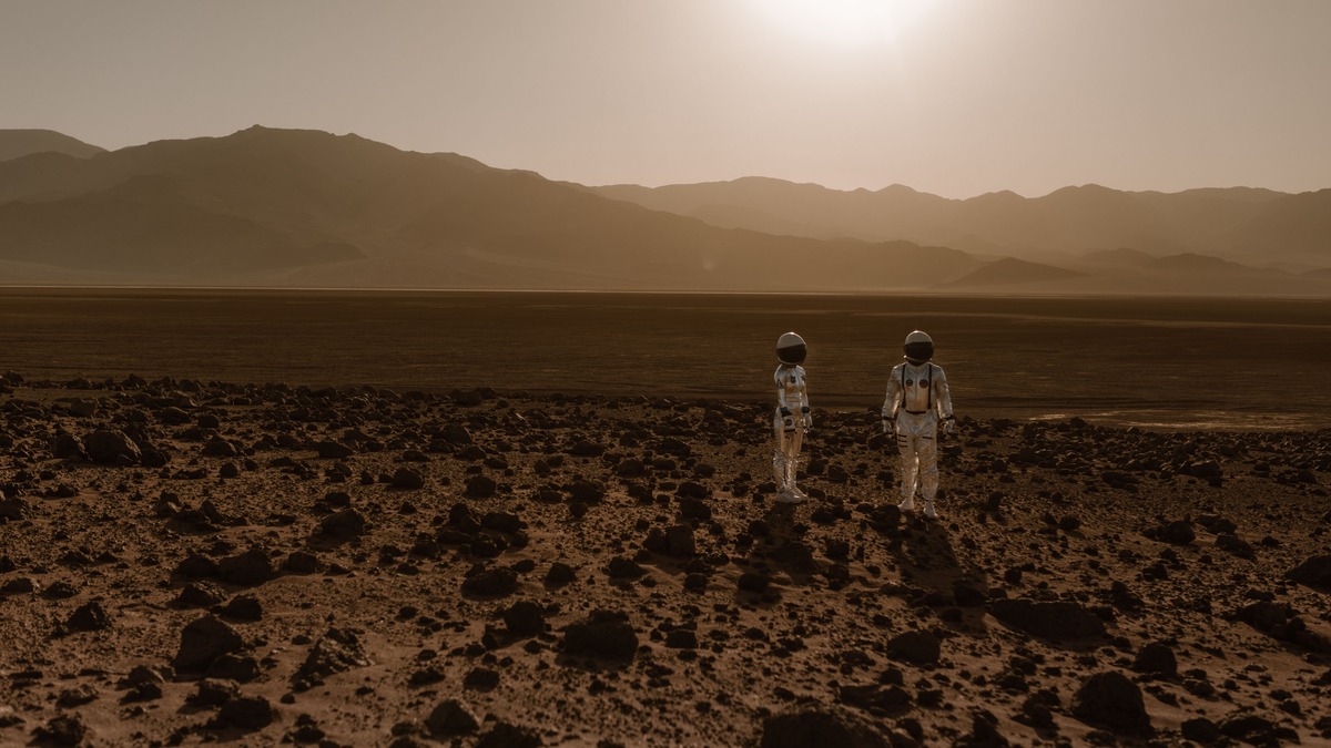 Astronauts in space suits explore a rocky, desert-like terrain resembling Mars at sunset