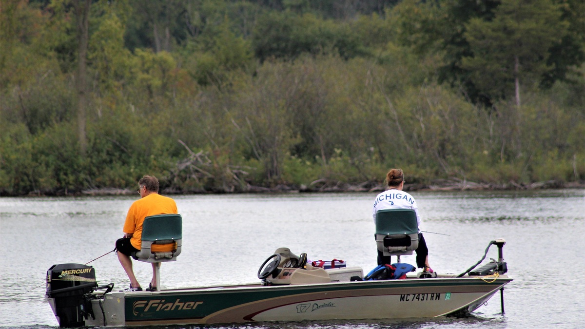 A couple leisurely fishing on a Michigan lake from a motorboat, surrounded by nature