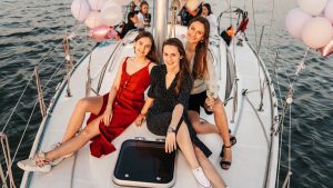 Three women celebrate on a yacht at sunset, enjoying a cheerful and memorable time
