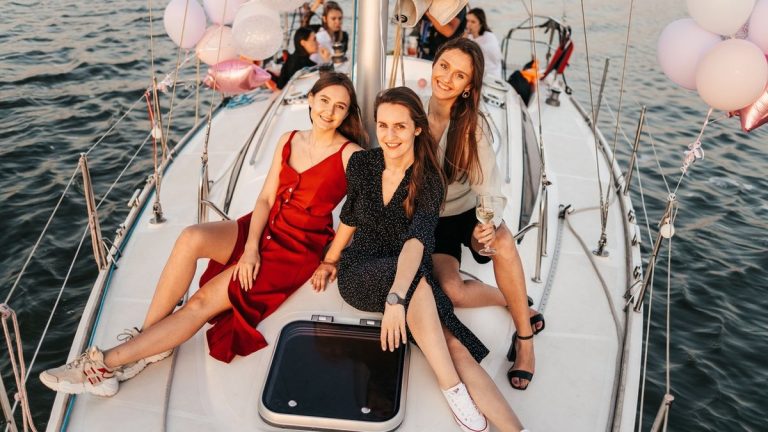 Three women celebrate on a yacht at sunset, enjoying a cheerful and memorable time