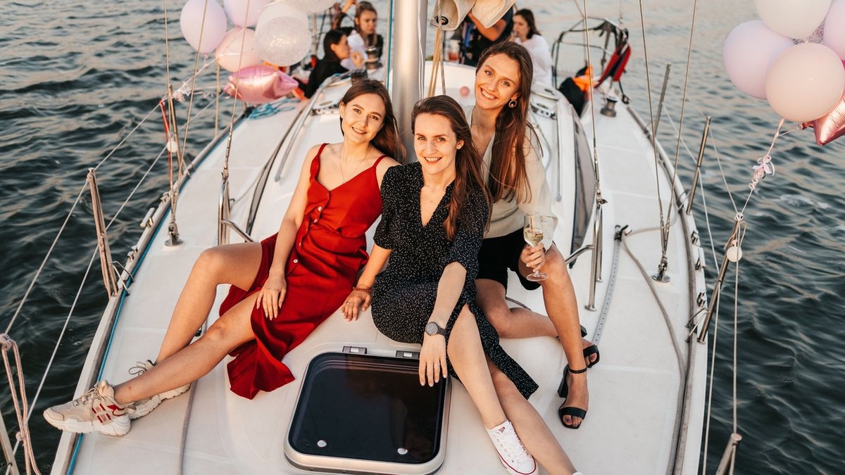 Three women celebrate on a yacht at sunset, enjoying a cheerful and memorable time