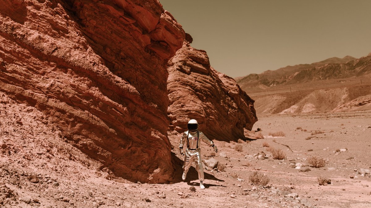 An astronaut in a spacesuit explores a barren, eroded desert, resembling Martian terrain