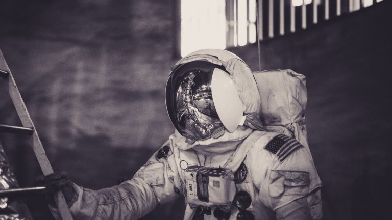 Astronaut in spacesuit climbing ladder inside a dark setting