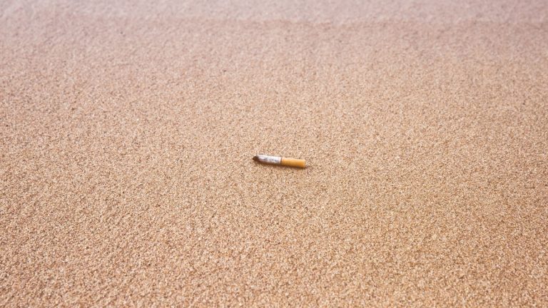 Cigarette butt discarded on a sandy beach, highlighting pollution