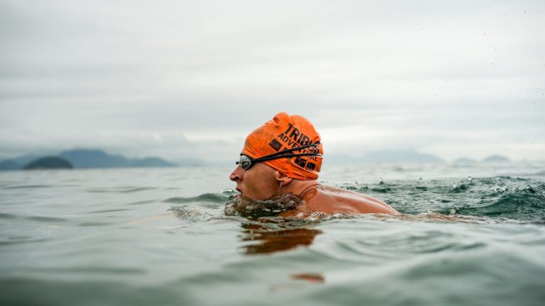 Adult male swimmer in open water wearing an orange swim cap and goggles, swimming in the sea