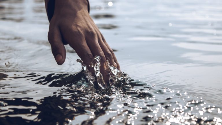 A serene close-up of a hand gently touching a sparkling water surface under daylight