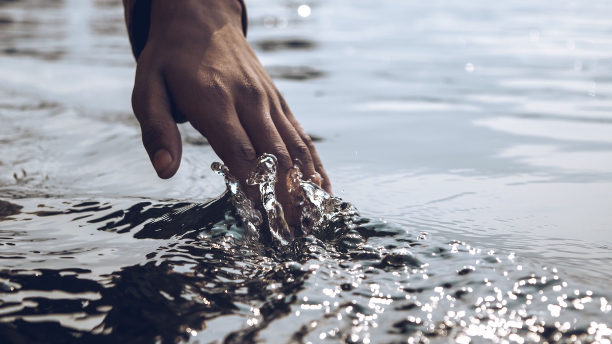 A serene close-up of a hand gently touching a sparkling water surface under daylight