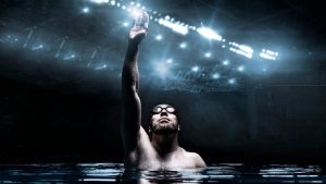 Swimmer in the pool raises his hands up. Water Sports Victory Concept. Arena with flashes. Mixed media