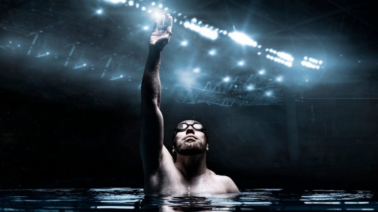Swimmer in the pool raises his hands up. Water Sports Victory Concept. Arena with flashes. Mixed media