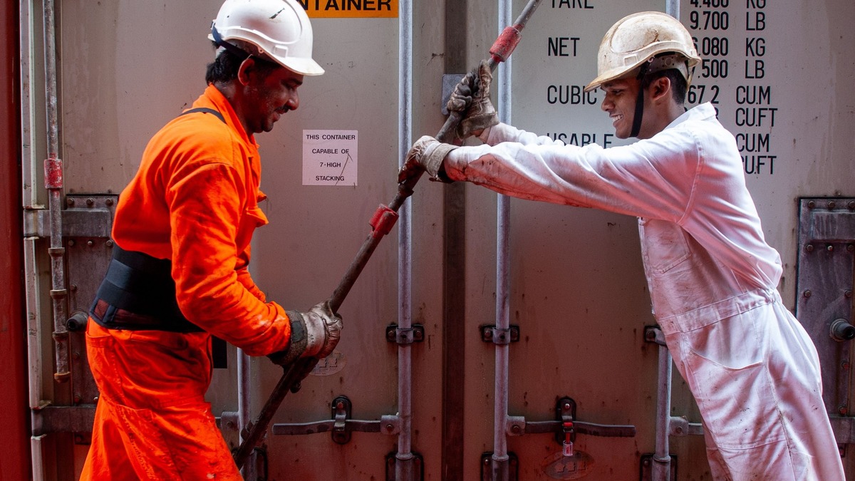 Two dockworkers securing a container on a ship, emphasizing teamwork and safety