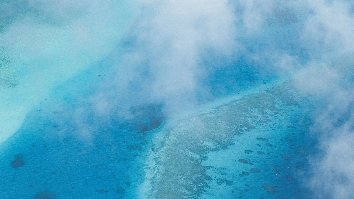 Stunning aerial view of a coral reef submerged in a vibrant blue ocean under scattered clouds